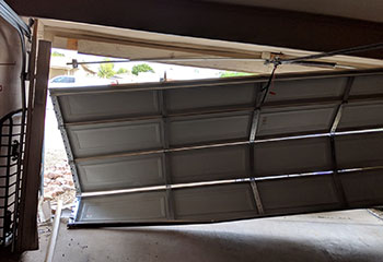 Severely damaged and misaligned sectional garage door before replacement at a Shakopee, MN residential property.